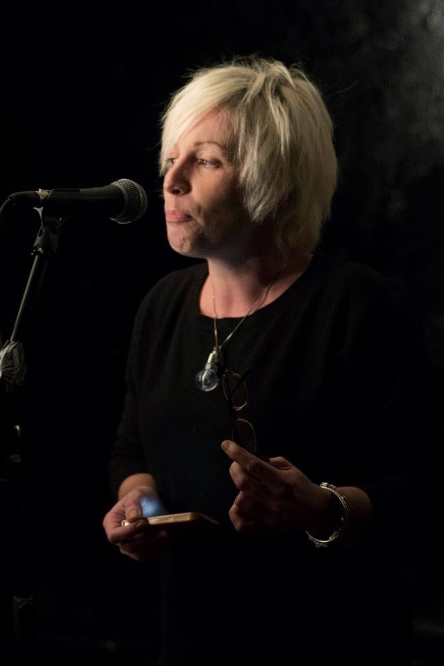 Sara performing at mic, with her phone in one hand and glasses in the other.