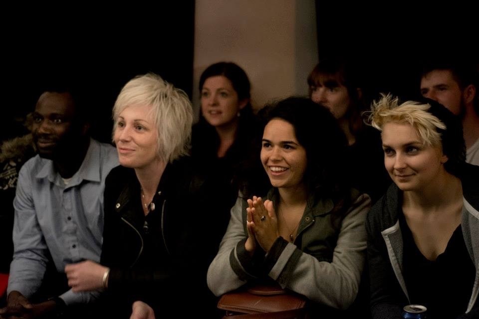 Sara and other poets in the audience, everyone is smiling at the performer.