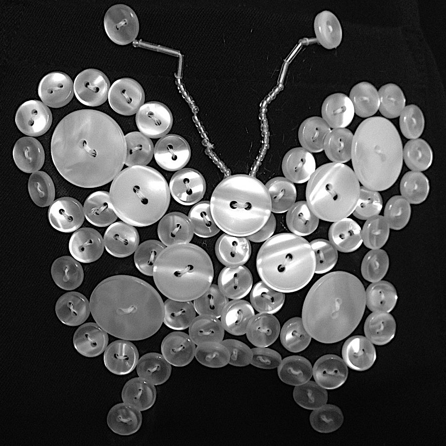 A butterfly made of pearl buttons sewn onto black fabric