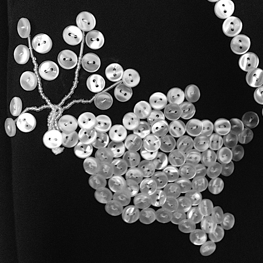 A peace dove with an olive branch in its beak made of pearl buttons sewn onto black fabric