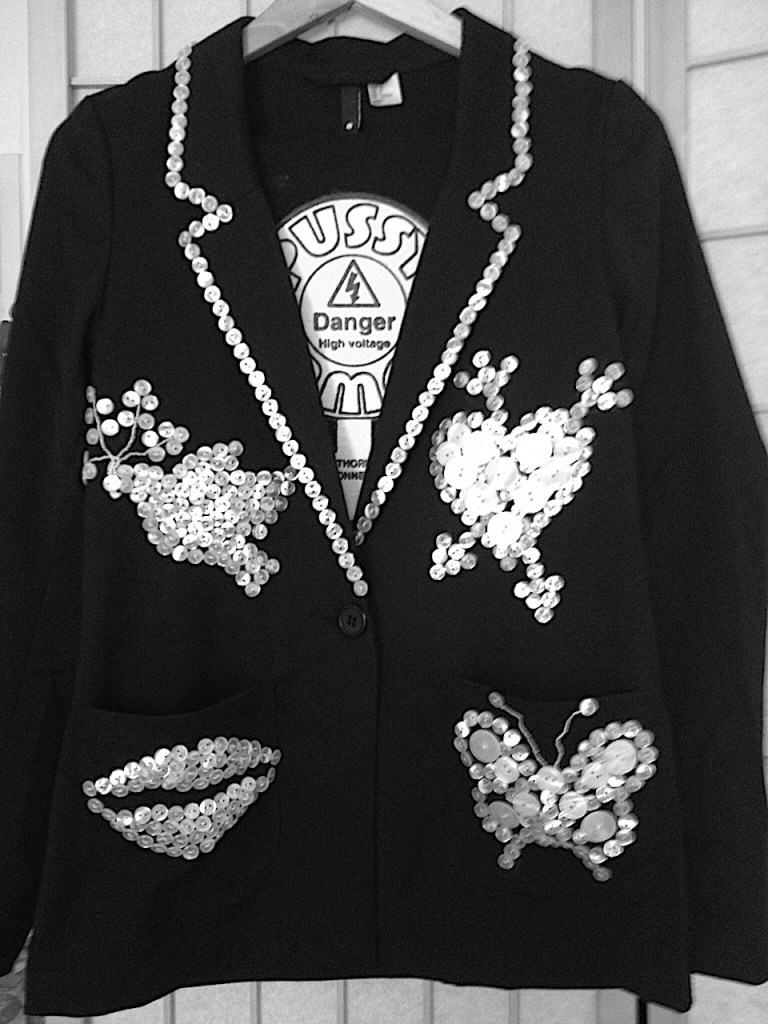 A design featuring a peace dove, a heart, a butterfly, and pouting lips, all made of pearl buttons sewn onto black fabric