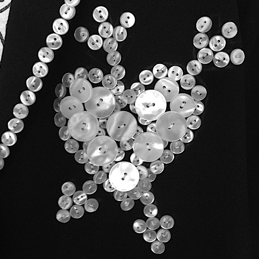 A heart with two arrows going through it made of pearl buttons sewn onto black fabric