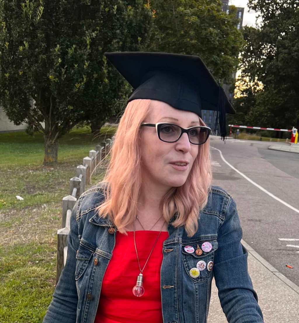 Sara after her graduation ceremony and complementary prosecco, wearing her mortarboard with her denim jacket and a necklace with lightbulb pendant