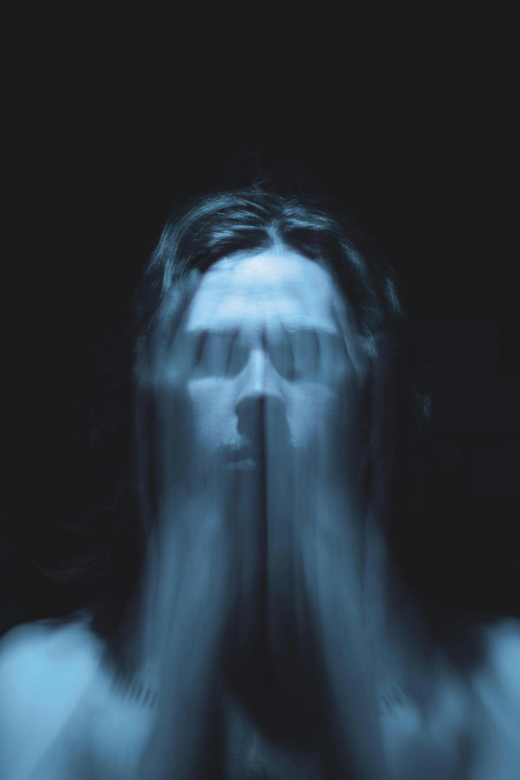 a man is pictured in a dark room, his hands are blurry as he moves them in front of his face