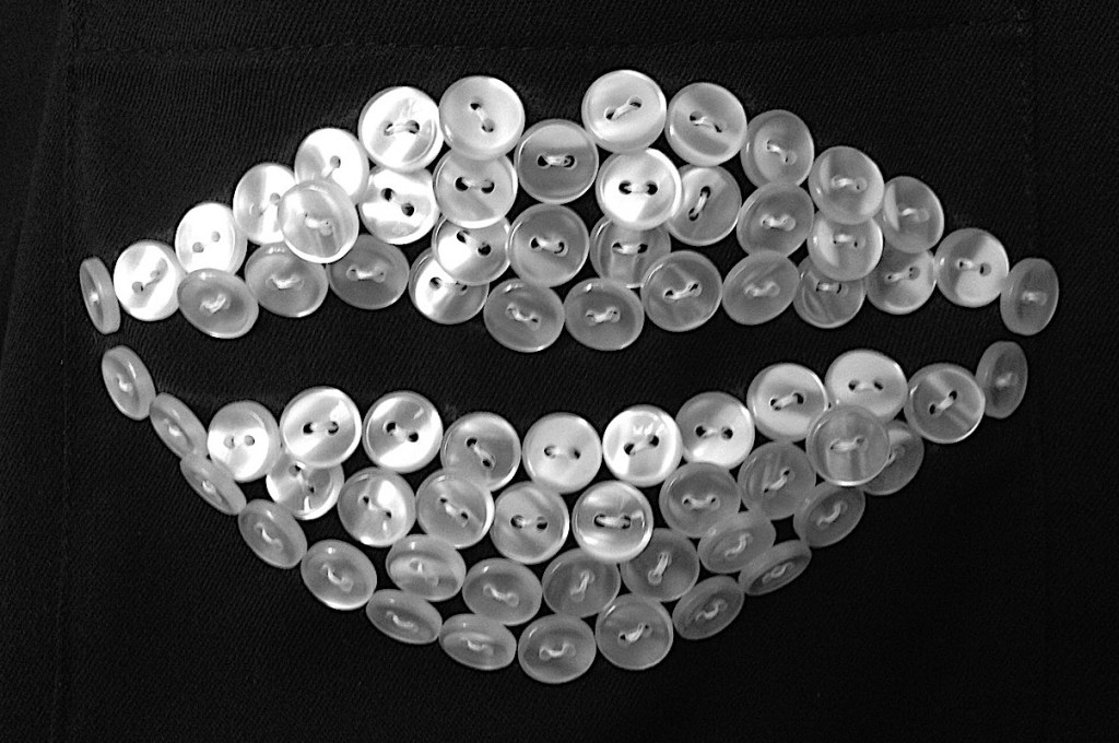 A pouting lips made of pearl buttons sewn onto black fabric